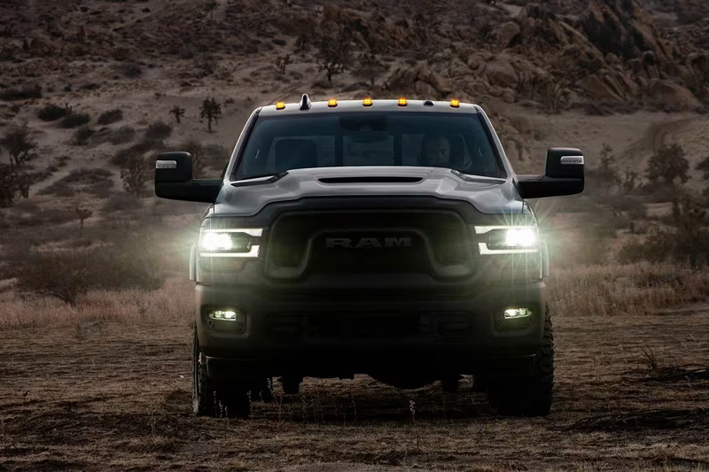 A head-on view of a 2023 Ram 2500 Rebel being driven off-road, in the desert at dusk, with its headlamps on