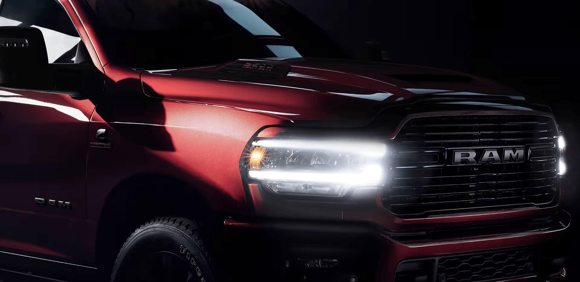 A close-up of the passenger-side front end of a red 2024 Ram 2500 Laramie with its Daytime Running Lamps and cornering lamps on.
